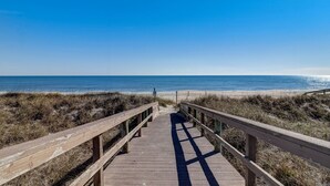 Une promenade en bois menant à une plage, avec un ciel dégagé.