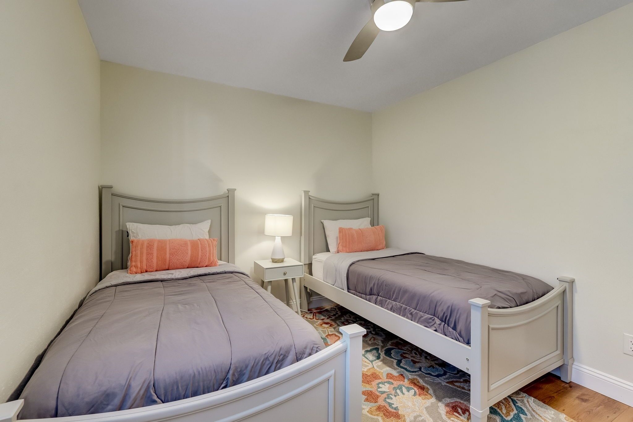 A bedroom with two single beds, a ceiling fan, and a nightstand with a lamp.