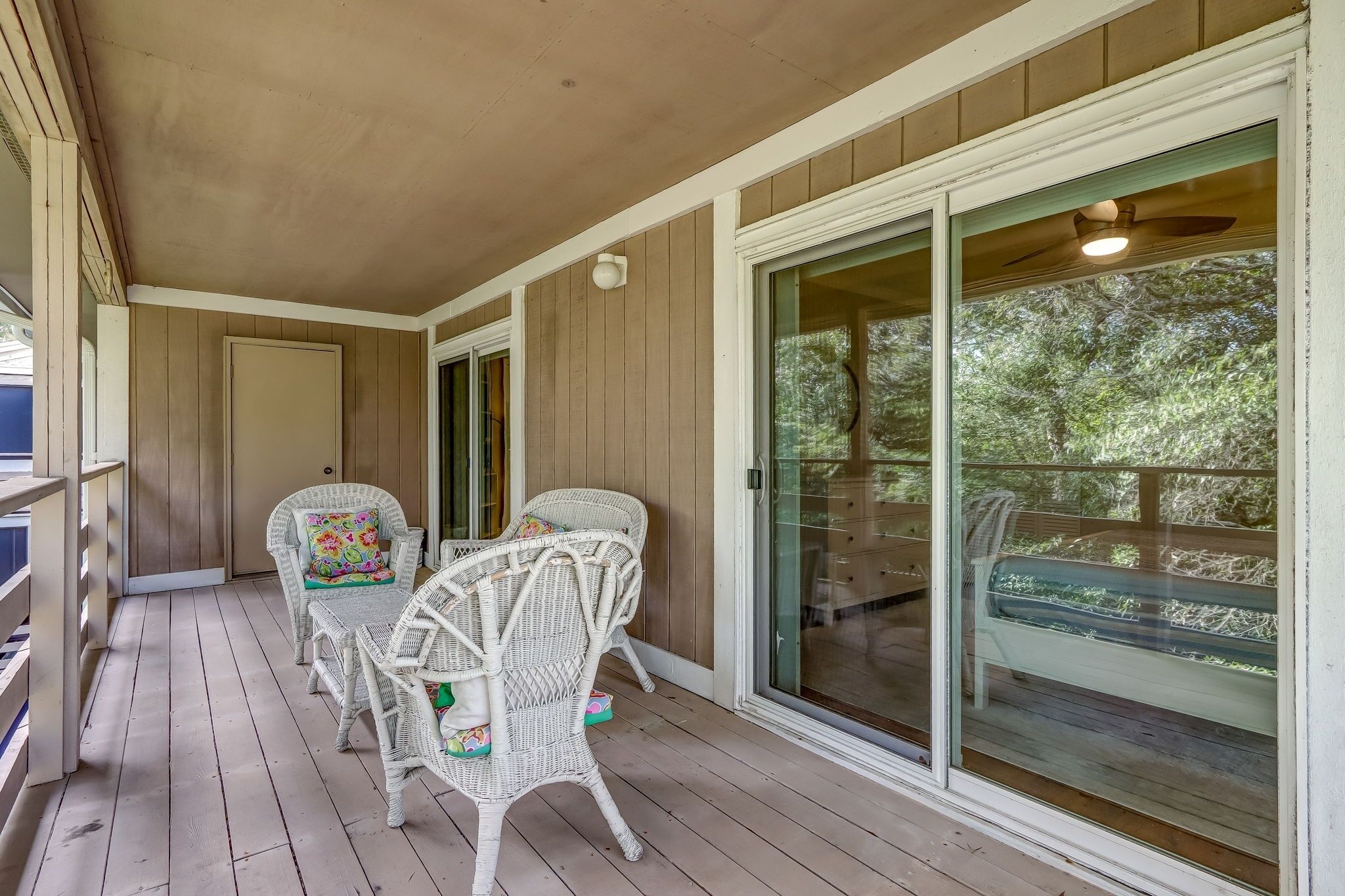 A covered porch with wicker chairs and a glass door leading to a deck.