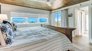 Un dormitorio con una cama grande, ventilador de techo y vista al océano a través de las ventanas.