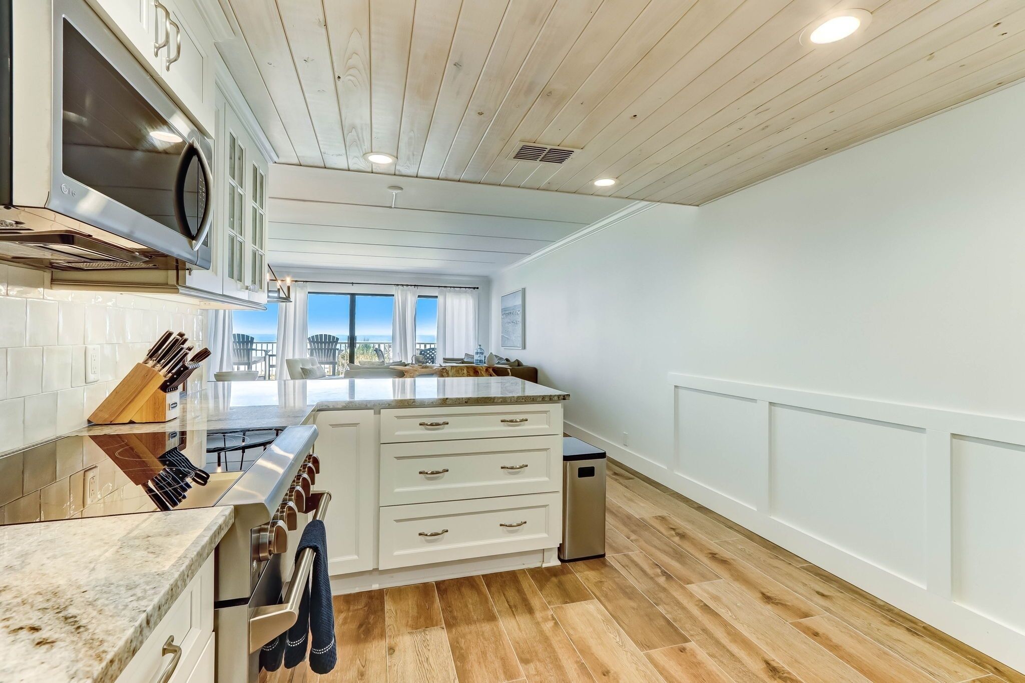 A modern kitchen with white cabinetry, a stainless steel stove, and a large island with a marble countertop.