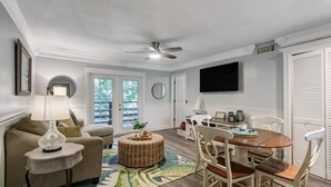 A well-lit living room with a ceiling fan, a dining area with a wooden table and chairs, and a TV mounted on the wall. - Fernandina Beach Hidden Gem Amelia Landings - 9F (Fernandina Beach)