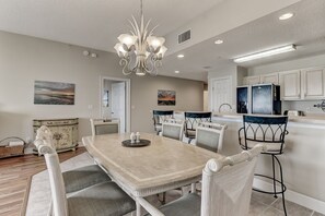 A dining area with a large marble table, six chairs, a chandelier, and artwork on the walls.