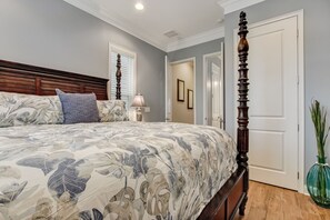 A bedroom with a large bed, a wooden headboard, a bedside lamp, and a green vase on the floor. - Haven across the Ocean - Pet Friendly 1931 S Fletcher (Fernandina Beach)