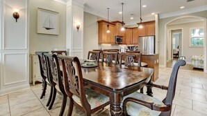 A dining area with a wooden table and chairs, a kitchen with wooden cabinets and stainless steel appliances, and a framed picture on the wall. - Haven across the Ocean - Pet Friendly 1931 S Fletcher (Fernandina Beach)