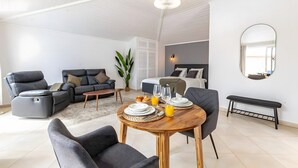 Moderni olohuone, jossa on ruokailutila, sohva, nojatuoli, sänky ja penkki.