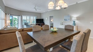 A dining area with a large wooden table, cushioned chairs, and a chandelier. - Stunning 3BR Condo w/ Wraparound Porch Ocean Park (Fernandina Beach)