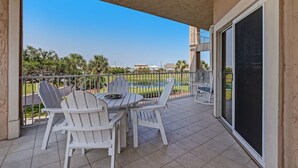 A balcony with a table and chairs, a view of a swimming pool, and a building in the background. - Stunning 3BR Condo w/ Wraparound Porch Ocean Park (Fernandina Beach)