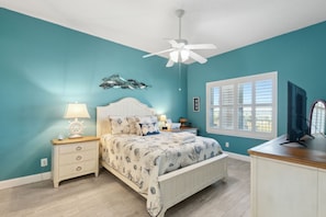 A bedroom with a bed, nightstand, lamp, ceiling fan, window, and TV. - Spacious 3BR Condo by The Beach Ocean Park - 106 (Fernandina Beach)