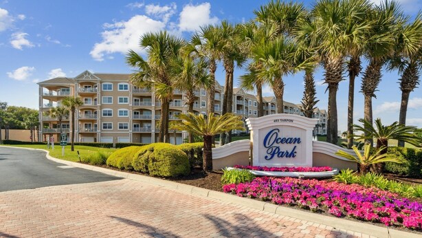 Un hotel de varios pisos con un letrero que dice 'Ocean Park' y una zona ajardinada con palmeras y flores.
