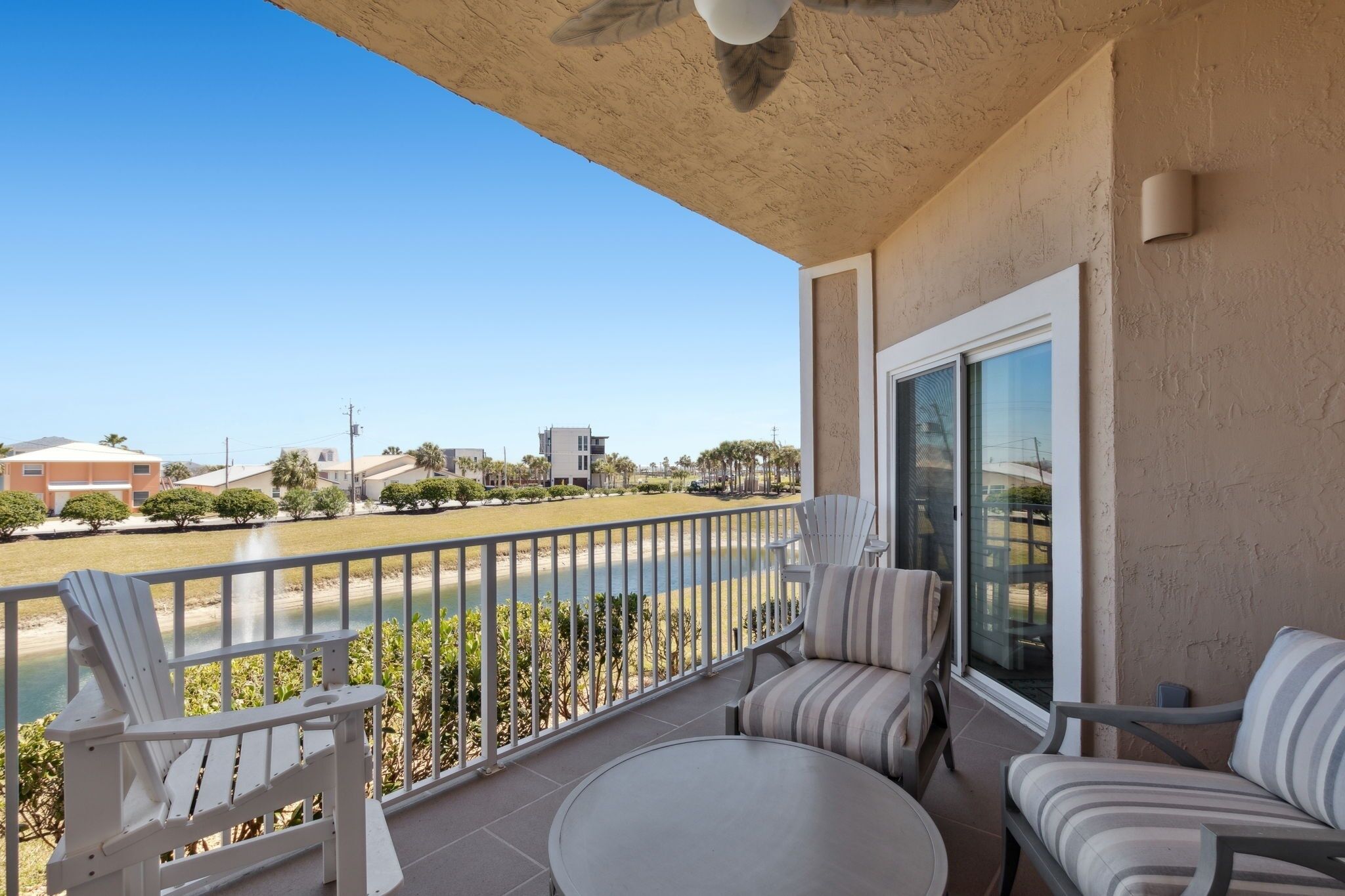 A balcony with a view of a beach and buildings, furnished with chairs and a table.