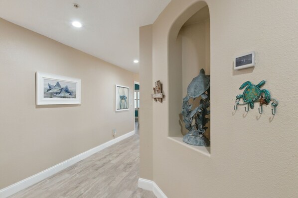 Un couloir aux murs de couleur beige, doté d’un parquet clair et agrémenté d’œuvres d’art, notamment un tableau encadré, un panneau d’accueil et une sculpture de tortue.