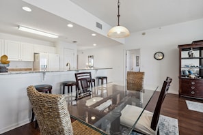 A modern kitchen with white cabinets, a glass dining table, and dark wooden chairs. - Sunshine Bliss at Fernandina Beach Ocean View, Pool, Hot Tub (Fernandina Beach)
