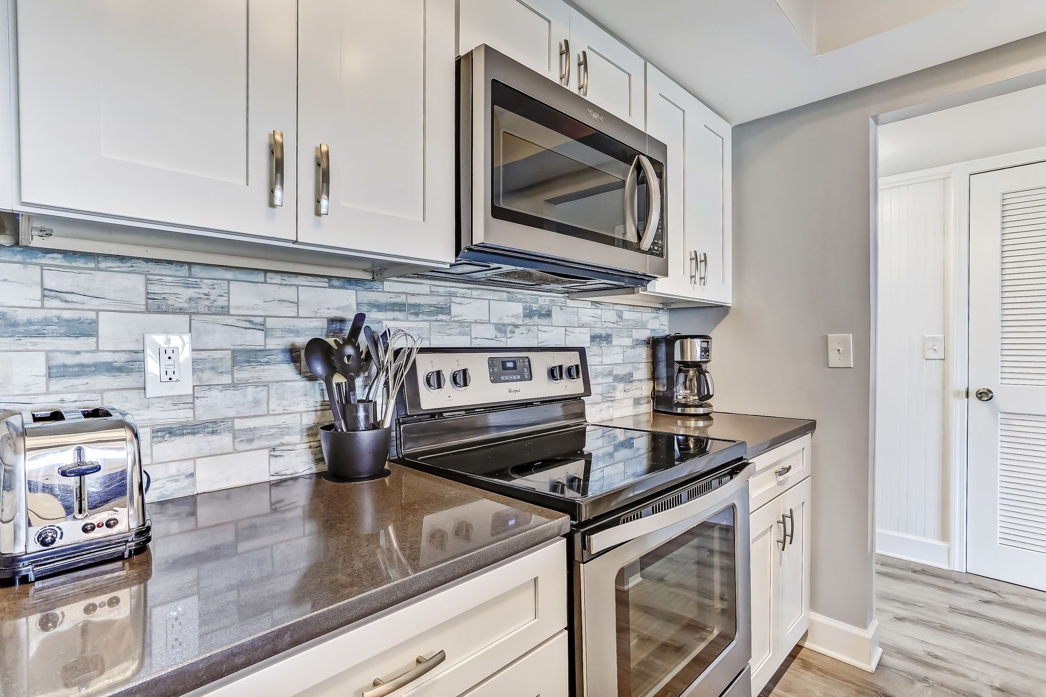 A modern kitchen with white cabinets, a stainless steel microwave, a gas stove, and a toaster.