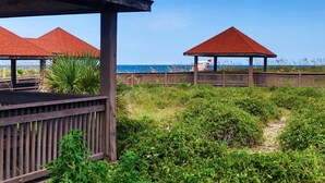Un pavillon situé au bord de la plage, doté d’une terrasse en bois et d’un toit rouge, entouré d’une végétation luxuriante et offrant une vue sur l’océan.