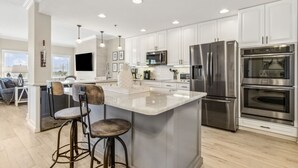 A modern kitchen with white cabinets, stainless steel appliances, and a central island with bar stools. - Luxury Private Beachfront Condo w/ Parking Garage & Stunning Views (Fernandina Beach)