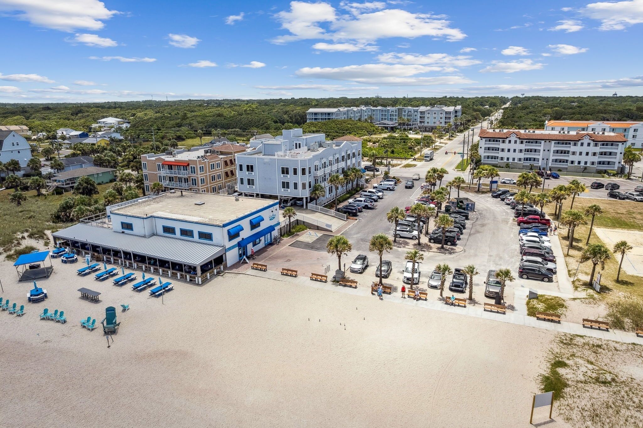 A hotel with a parking lot, beach chairs, and a view of the surrounding area.