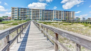 A wooden boardwalk leading to a multi-story hotel with balconies and a clear blue sky. - Beachfront Family Condo w/ Pool, Fishing, and Pier Access Amelia by the Sea (Fernandina Beach)