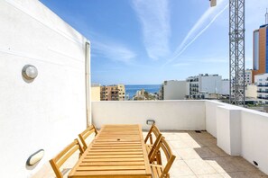 Una terraza en la azotea con una mesa y sillas de madera, una pared blanca y vistas a la ciudad y al mar.