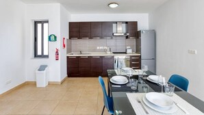 Une cuisine moderne avec des meubles en bois foncé, un réfrigérateur en acier inoxydable et un coin repas doté d’une table en verre, mise pour deux personnes.