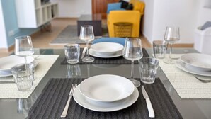 Une table à manger dressée avec de l’argenterie blanche, des couverts et des verres transparents, sur fond d’intérieur moderne.