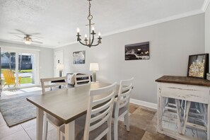 A dining area with a wooden table and white chairs, a chandelier, and artwork on the walls. - Tranquil Beach Retreat Fernandina Shores 6398 (Fernandina Beach)