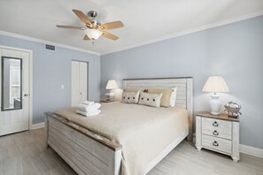 A bedroom with a bed, two bedside tables, a ceiling fan, and a door. - Tranquil Beach Retreat Fernandina Shores 6398 (Fernandina Beach)