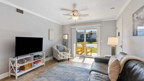 A living room with a flat-screen TV, a ceiling fan, a sofa, a chair, and a sliding glass door leading to an outdoor area. - Tranquil Beach Retreat Fernandina Shores 6398 (Fernandina Beach)