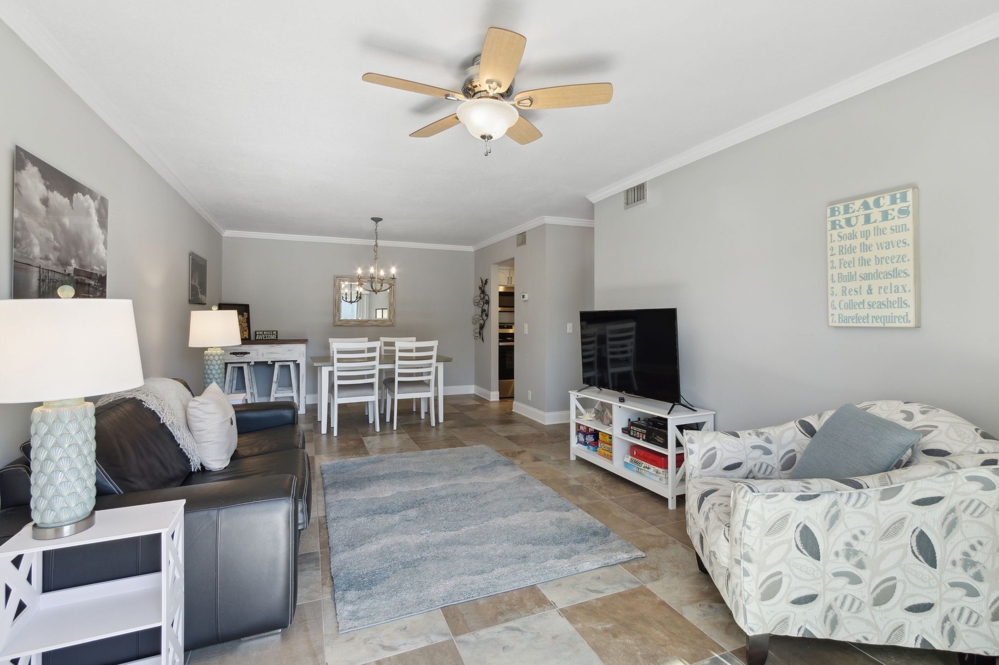 Ein modernes Wohnzimmer mit Deckenventilator, einem Essbereich mit einer Kronleuchter und einem Fernsehgerät auf einem weißen Schrank.