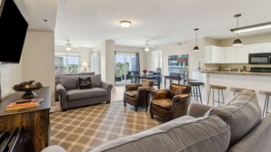 A modern living room with a sofa, armchairs, and a coffee table. There is a flat-screen TV mounted on the wall, a dining area with a table and chairs, and a kitchen with a microwave and bar stools. - Tranquil 1BR Getaway in Fernandina Beach - Ocean View (Fernandina Beach)
