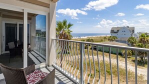 A balcony with a view of the beach and ocean, furnished with wicker chairs and a table. - Tranquil 1BR Getaway in Fernandina Beach - Ocean View (Fernandina Beach)
