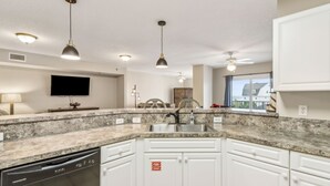A modern kitchen with granite countertops, white cabinetry, a built-in dishwasher, pendant lighting, and a large window providing natural light. - Tranquil 1BR Getaway in Fernandina Beach - Ocean View (Fernandina Beach)