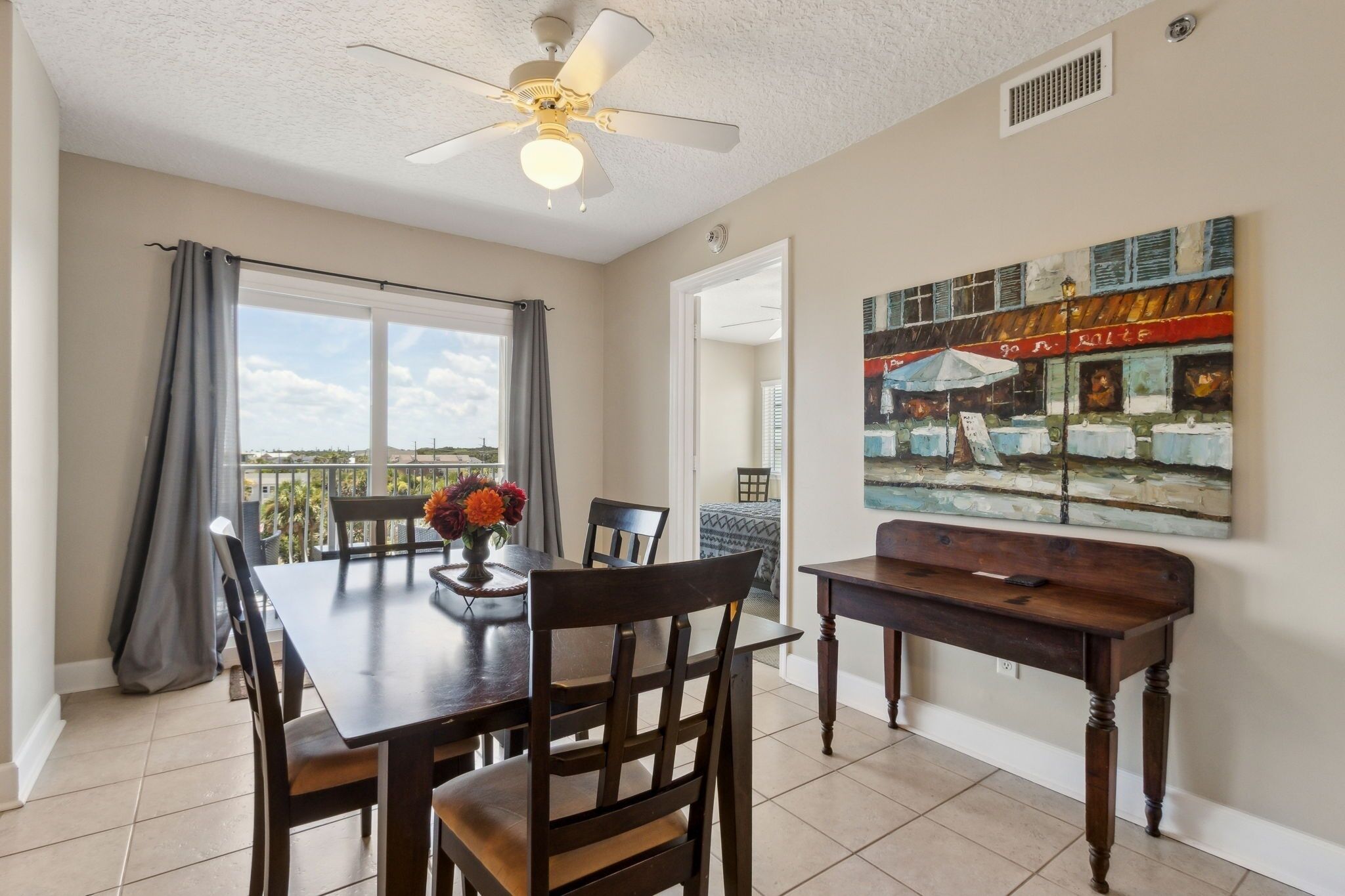 A dining area with a table, chairs, a ceiling fan, and a painting on the wall.