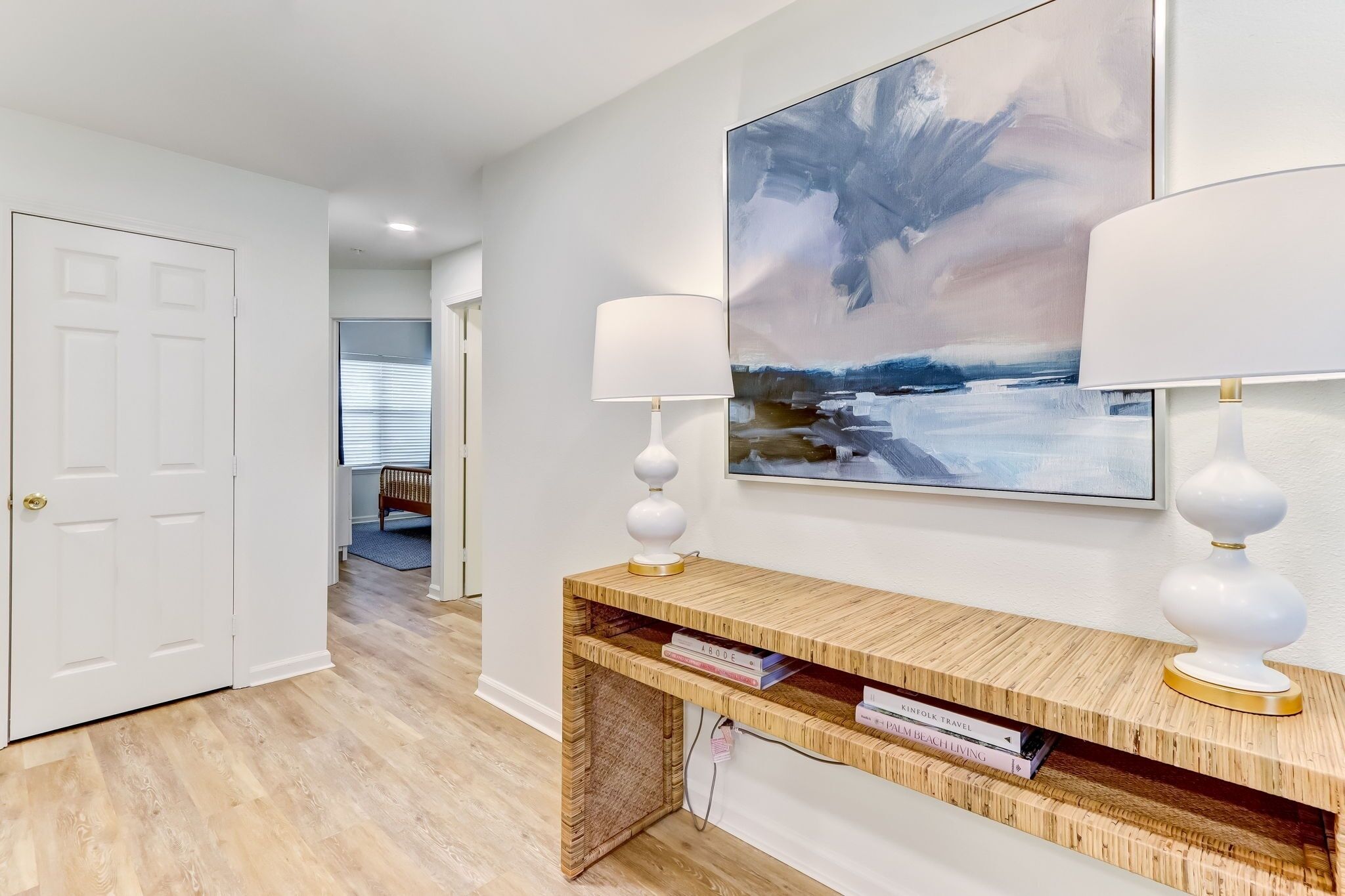 A hallway with a wooden console table, two white lamps, and a large abstract painting on the wall.