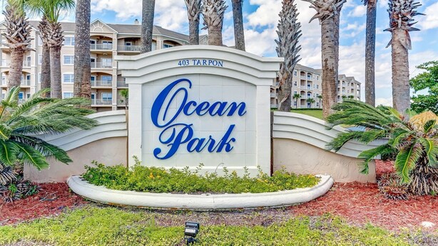 Un letrero indica Ocean Park, un edificio de varios pisos con balcones, rodeado de palmeras y jardines.