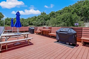 Une terrasse en bois avec des tables de pique-nique et des parasols bleus, un barbecue et un panneau indiquant qu’il s’agit d’une zone protégée.