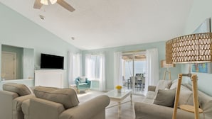 A living room with beige sofas, a coffee table, and a television on the wall. - North End Gem - Pet Friendly Fernandina Beach Cottage (Fernandina Beach)