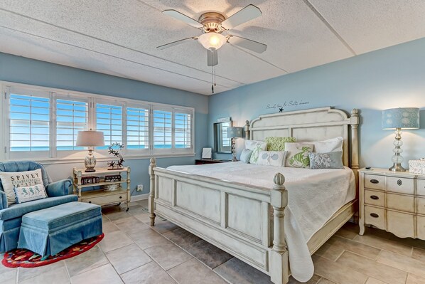 A bedroom with a bed, a chair, a nightstand, a lamp, and a ceiling fan. - Beachfront 6th floor Condo w/ Ocean View Amelia by the Sea (Fernandina Beach)