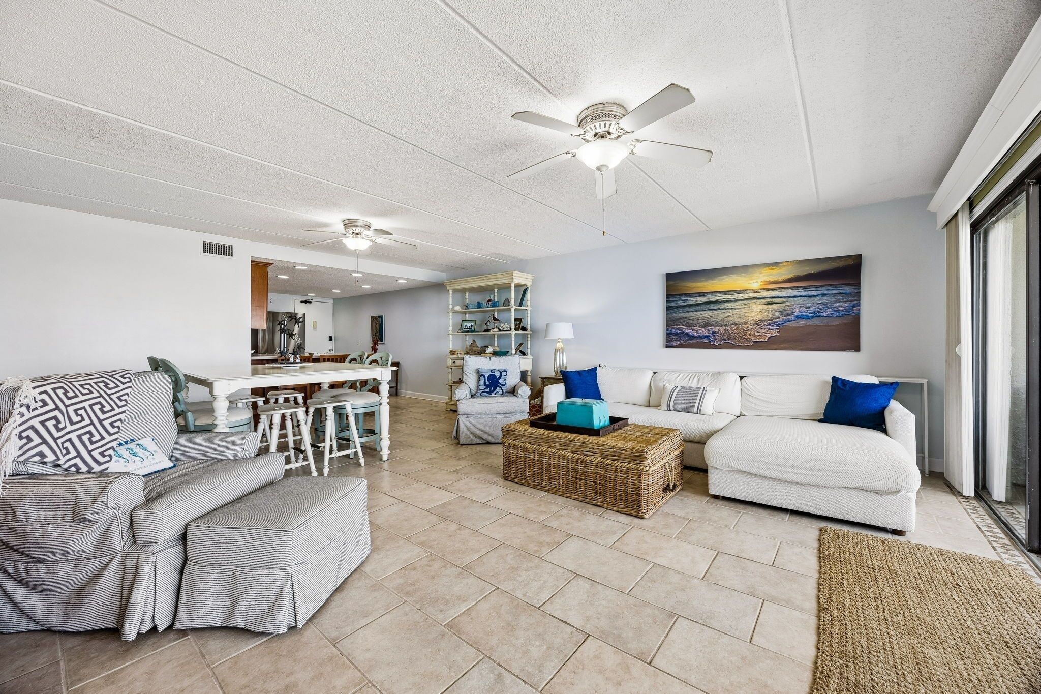 A spacious living area with a dining table, two sofas, a ceiling fan, and a large window with a view.