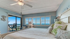 Une chambre dotée d’un grand lit, d’un ventilateur de plafond et offrant une vue sur l’océan grâce à une porte-fenêtre coulissante.