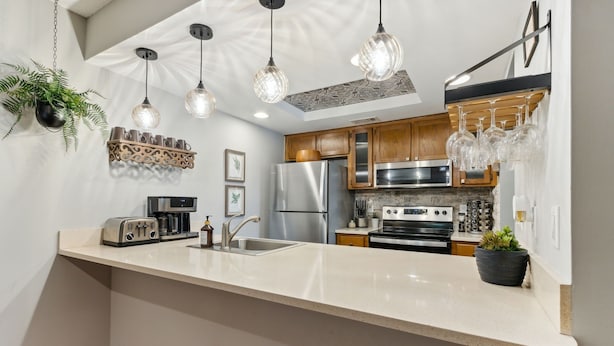A modern kitchen with stainless steel appliances, a white countertop, hanging pendant lights, and wooden cabinets. - Newly Renovated 2BR by the Beach Amelia Island (Fernandina Beach)