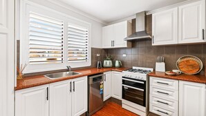 Una cocina moderna con armarios blancos, un lavamanos de acero inoxidable, una estufa a gas y un horno empotrado.
