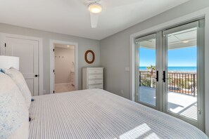 A bedroom with a bed, a dresser, a mirror, and a sliding glass door leading to a balcony with a view of the ocean. - Beachfront Luxury Home w/ Private Pool (Fernandina Beach)