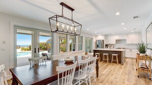 A modern kitchen with white cabinets, a wooden dining table, and a view of a swimming pool. - Beachfront Luxury Home w/ Private Pool (Fernandina Beach)