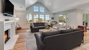 A spacious living room with a fireplace, large windows, and a high ceiling. - Beachfront Luxury Home w/ Private Pool (Fernandina Beach)