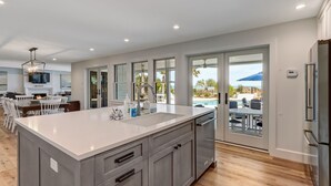 A spacious kitchen with a large island, a built-in oven, and a refrigerator. There is a dining area with a table and chairs, and a view of a pool and outdoor seating. - Beachfront Luxury Home w/ Private Pool (Fernandina Beach)