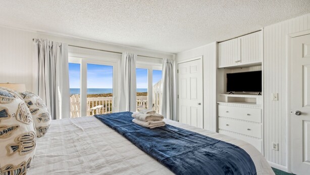 Een hotelkamer met een bed, een televisie en uitzicht op het strand.