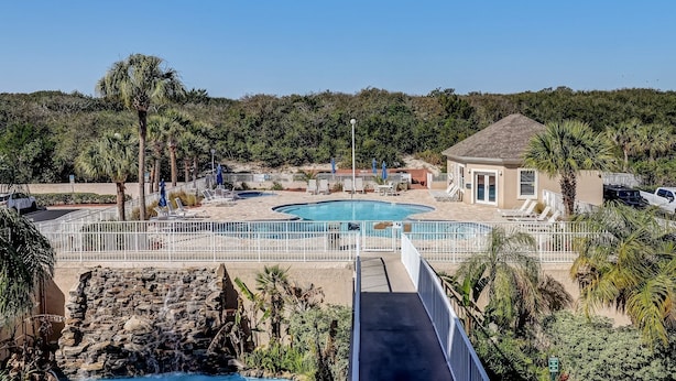 Un área de piscina con una piscina circular, sillas de descanso y un edificio pequeño.