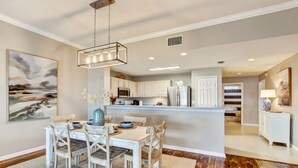 Una cocina moderna con armarios blancos, una isla central y un comedor con sillas y una mesa de madera.