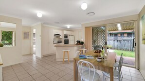A modern kitchen with white cabinets, a central island, and a dining area with a wooden table and white chairs.